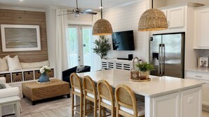 A modern kitchen with a central island, wooden chairs, and pendant lighting. - Seas the Day 30A - 6 Seater Golf Cart, 2 Pools, Beach Chairs, Wi-Fi & AC (Panama City Beach)