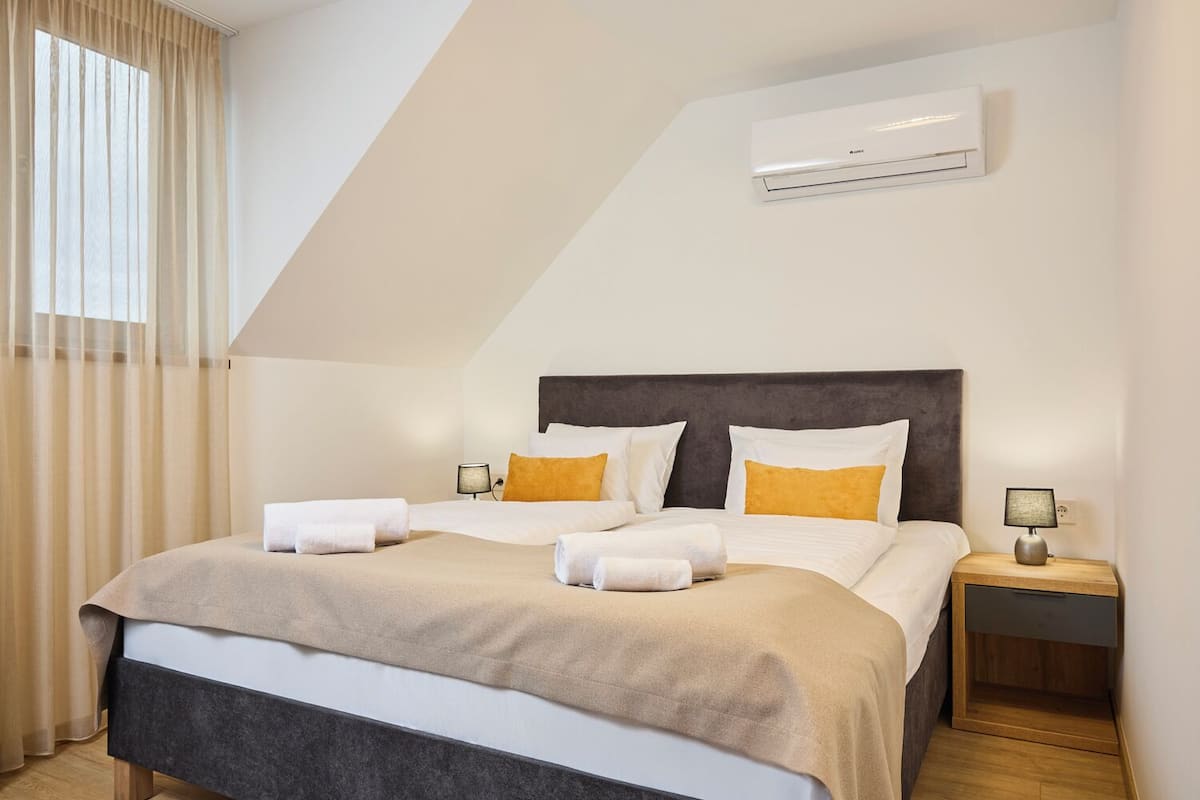 Une chambre d’hôtel avec un lit, deux tables de chevet, un appareil de climatisation et une fenêtre avec des rideaux.