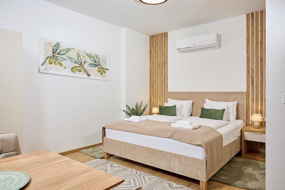 Une chambre d’hôtel comprenant un lit, des tables de chevet, un climatiseur fixé au mur, un mur recouvert de panneaux en bois et une œuvre d’art encadrée.
