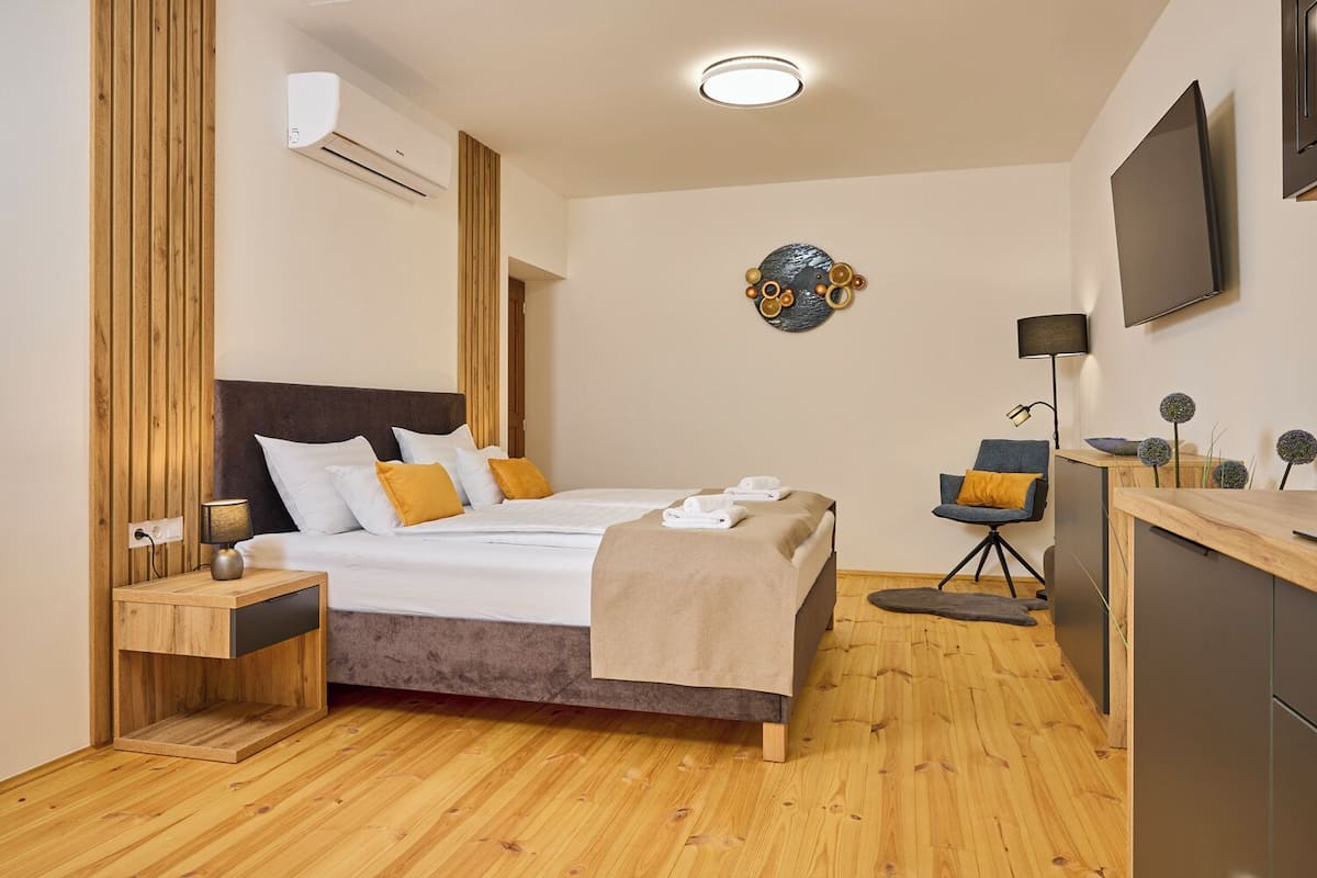 Une chambre d’hôtel moderne avec un plancher en bois, un lit avec une literie blanche et jaune, un bureau avec une chaise, un téléviseur à écran plat et un élément décoratif mural.