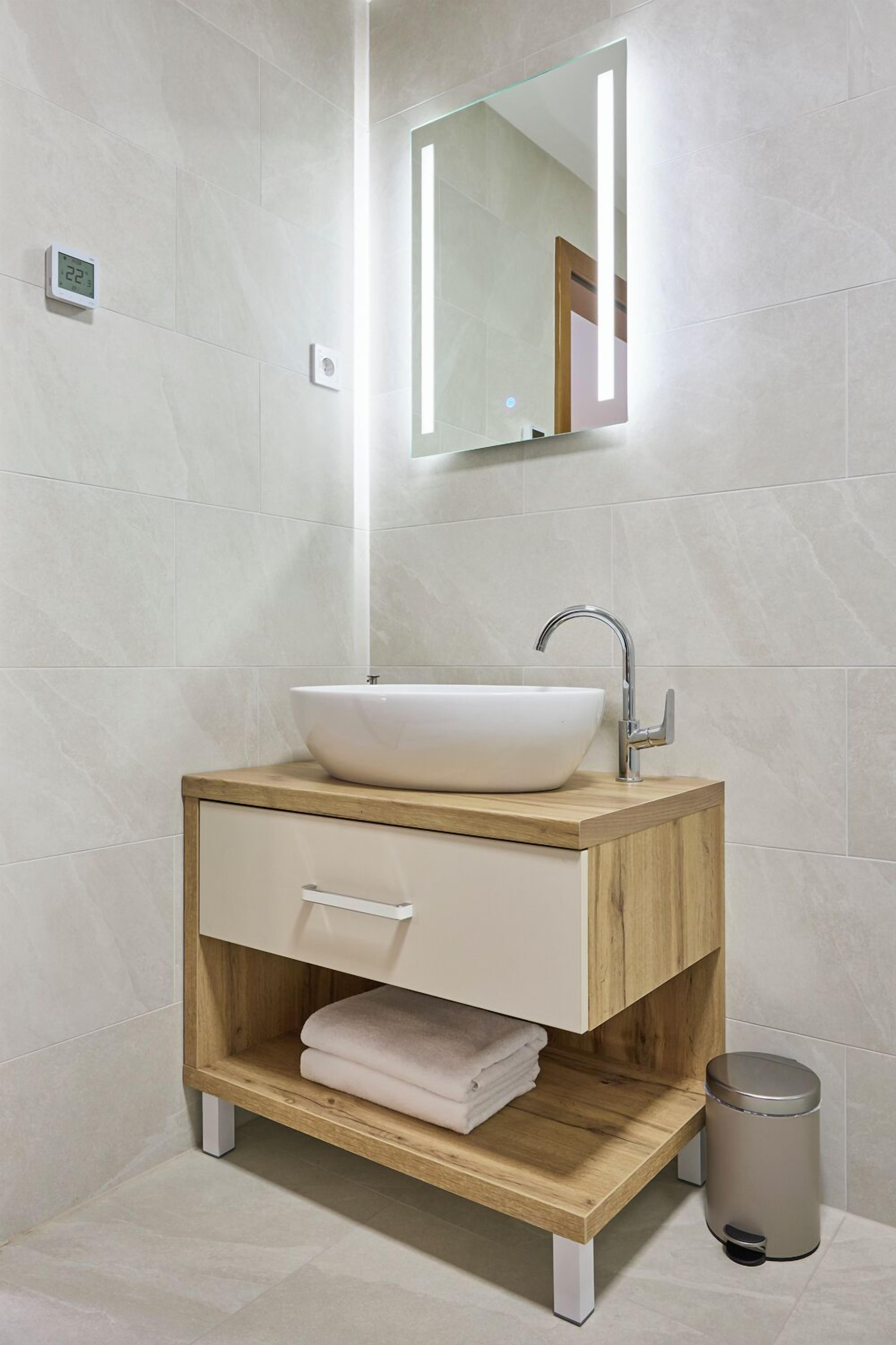 Un baño moderno con un lavabo tipo recipiente blanco, tocador de madera y espejo.