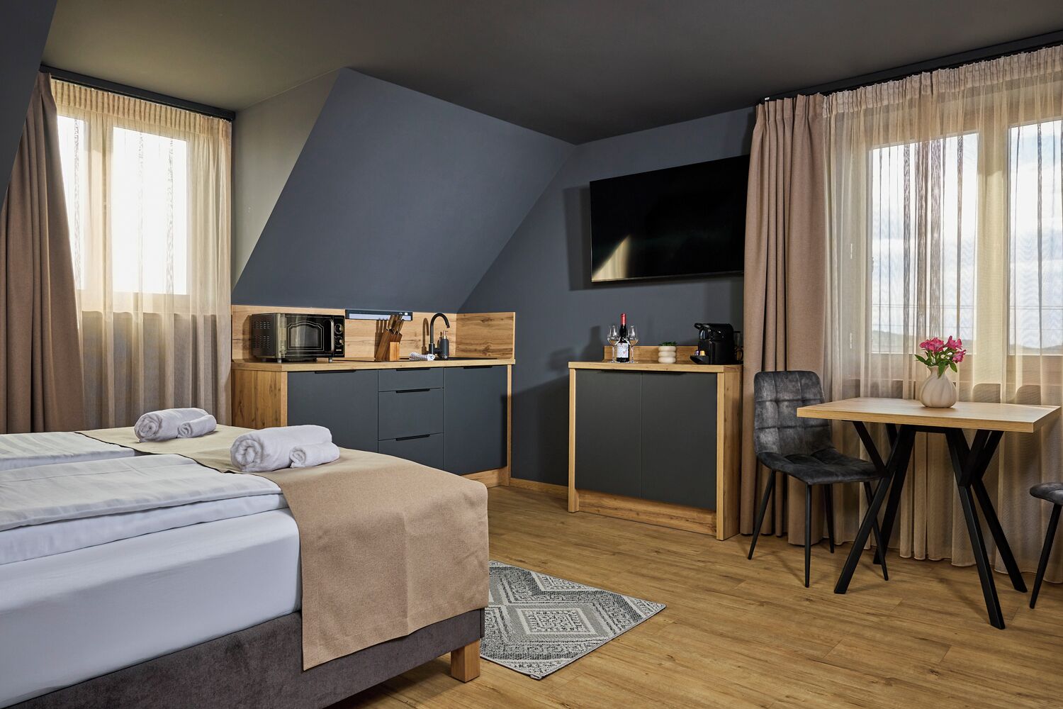Ein modernes Hotelzimmer mit Bett, Schreibtisch, Stuhl, Fernseher und einer Küchenzeile.