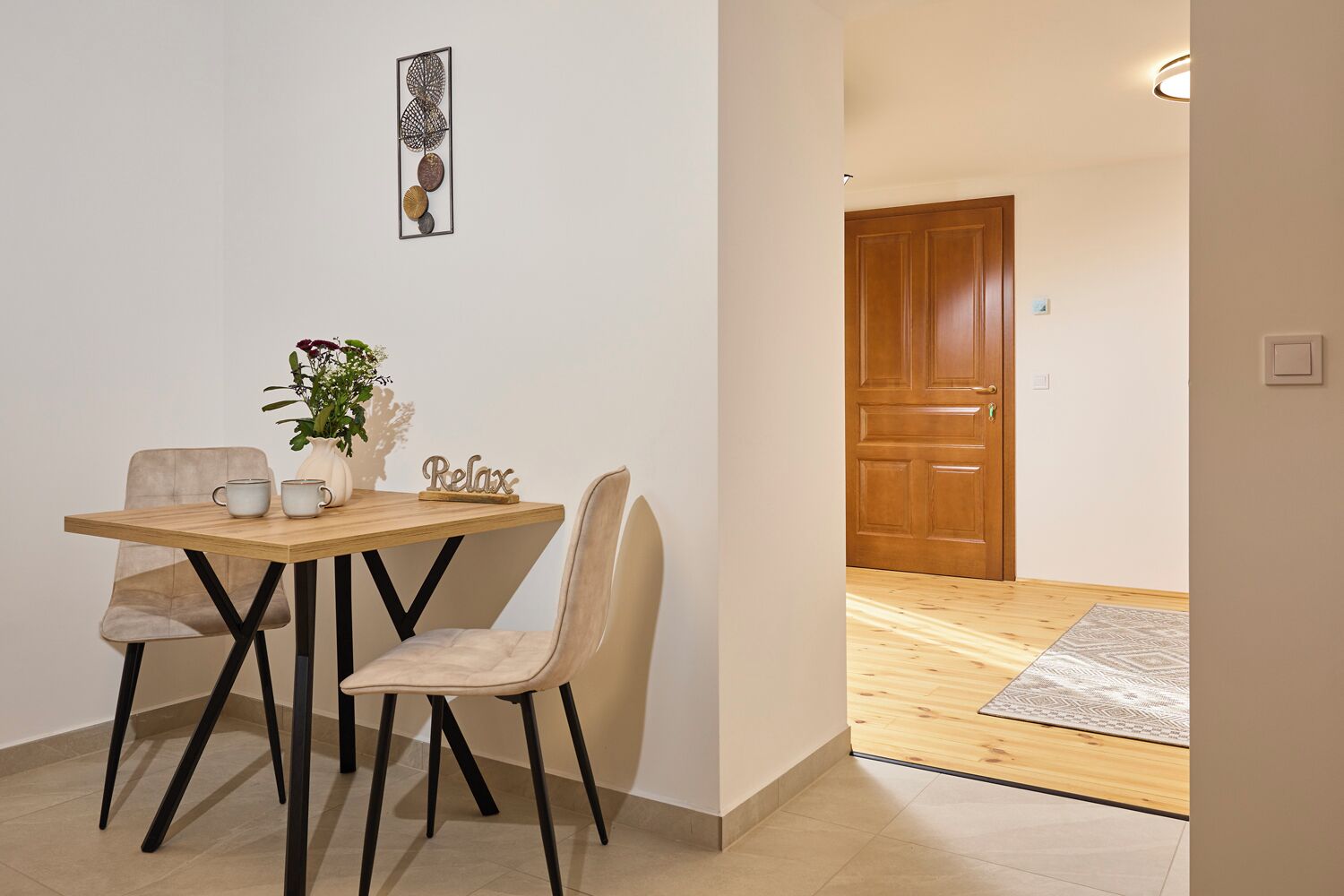 Un comedor con una mesa de madera, dos sillas, un florero con flores y una obra de arte colgada en la pared.