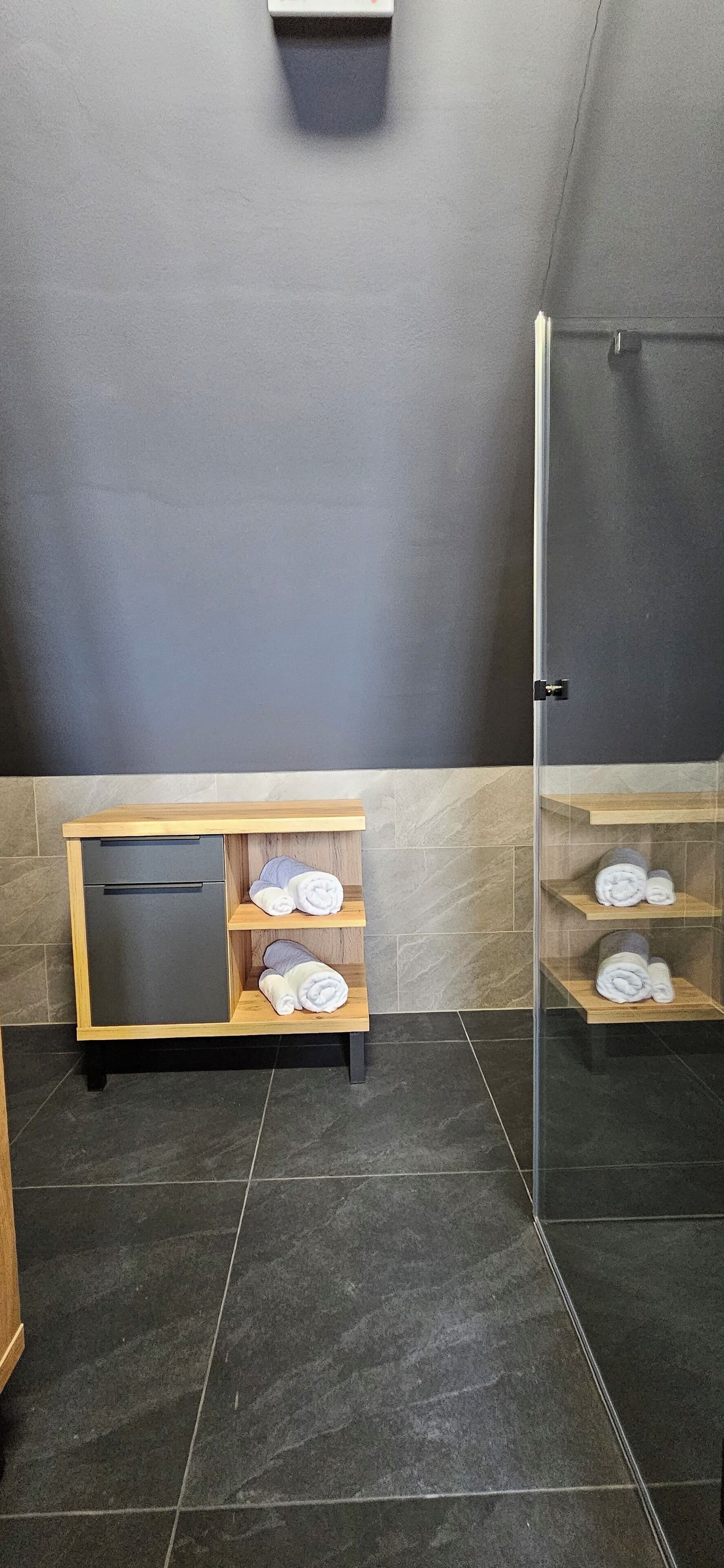Ein Badezimmer mit Dusche, einem Holzschrank mit Handtüchern und einer Glasdusche.