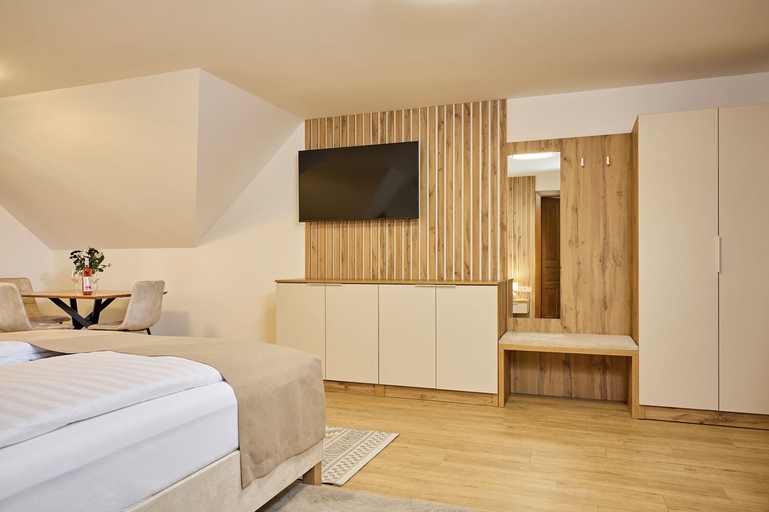 Une chambre moderne avec un lit, un bureau et un téléviseur fixé au mur, qui est en bois.