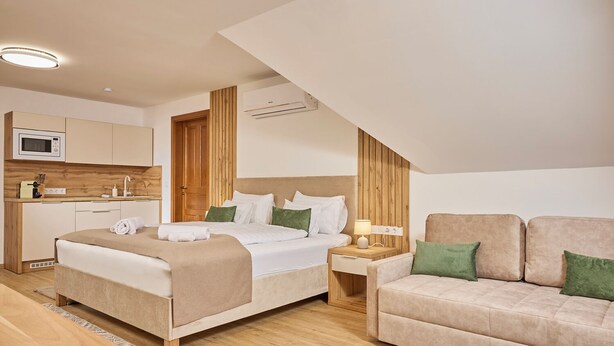 A modern bedroom with a bed, a nightstand, a sofa, and a kitchenette. - Villa Olea (Tihany)