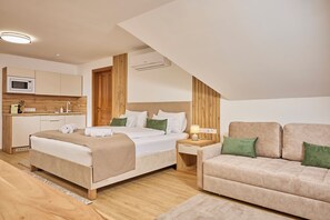 A modern bedroom with a bed, a nightstand, a sofa, and a kitchenette.