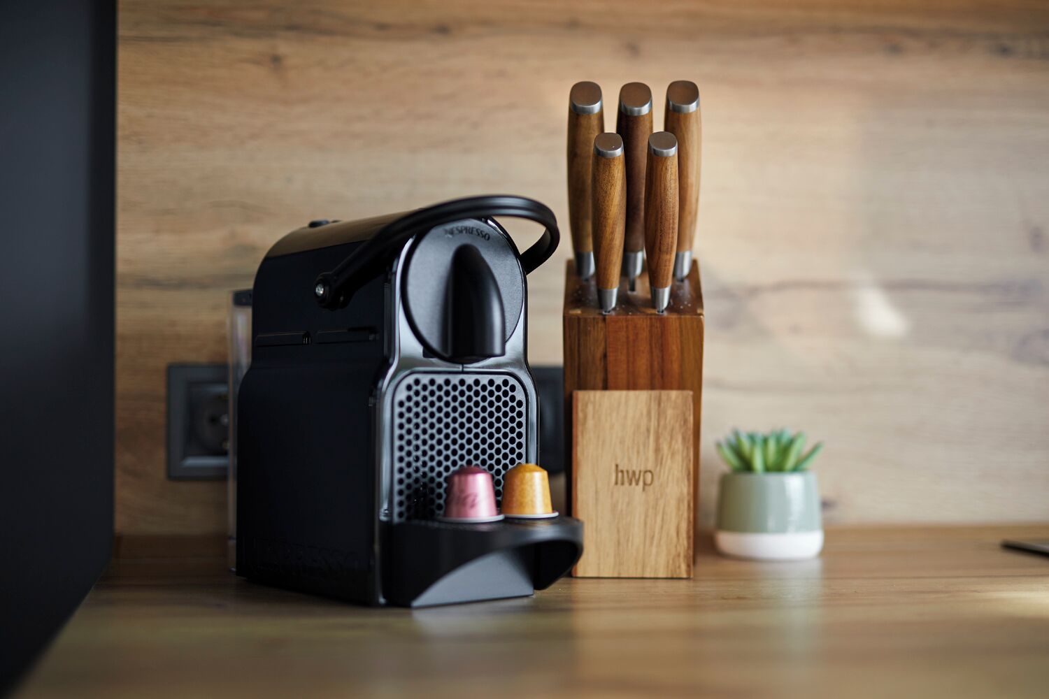 A coffee machine with a drip tray, a knife block, and a small potted plant on a wooden surface.