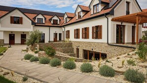 A modern house with a stone foundation, multiple windows with shutters, and a paved driveway. - Villa Olea (Tihany)