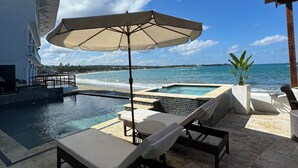 A poolside area with lounge chairs and an umbrella, overlooking a beach and ocean. - Ultra Infinity Hotel (Cabarete)