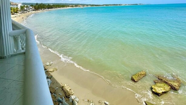 A beach view from a covered balcony with clear turquoise water and a sandy shoreline. - Ultra Infinity Hotel (Cabarete)