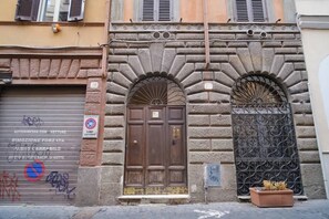 A building facade with a closed shutter, a metal gate, and a potted plant. - BuddyRent - Terrazza - Monti - 4 ospiti (Roma)