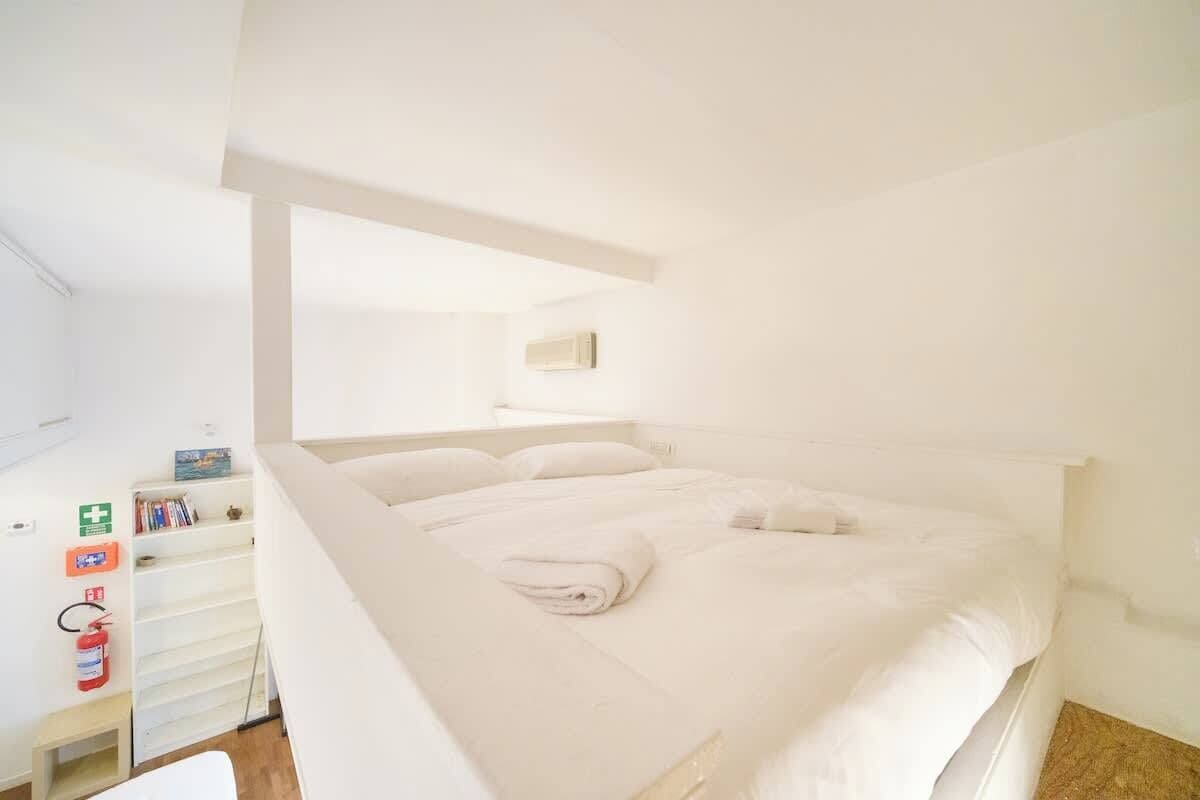 A white room with a bed, a white wardrobe, and a white shelf with books.