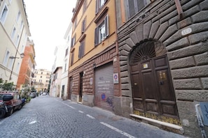 A cobblestone street with historic buildings, a closed shuttered door, and a parked vehicle.