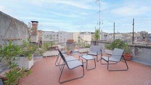 A rooftop terrace with outdoor seating, potted plants, and a view of the cityscape.