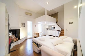 A bedroom with a large bed, a fireplace, a desk, and a staircase leading to an upper level.