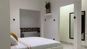 A modern bedroom with a bed, a nightstand, a potted plant, and a bathroom with a mirror and tiled floor.