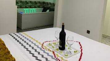Una habitación ordenada con una cama, una mesita con una botella y vasos, y una guirnalda decorativa.