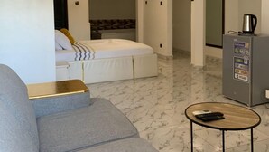 A modern living room with a grey sofa, a small coffee table, and a bed with a patterned headboard.