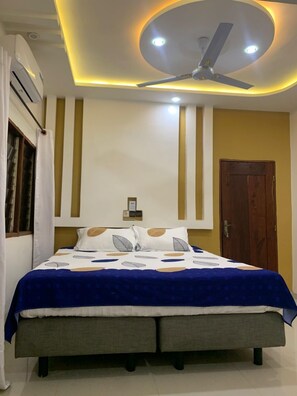 Een slaapkamer met een bed, een plafondventilator, inbouwverlichting en een houten deur.