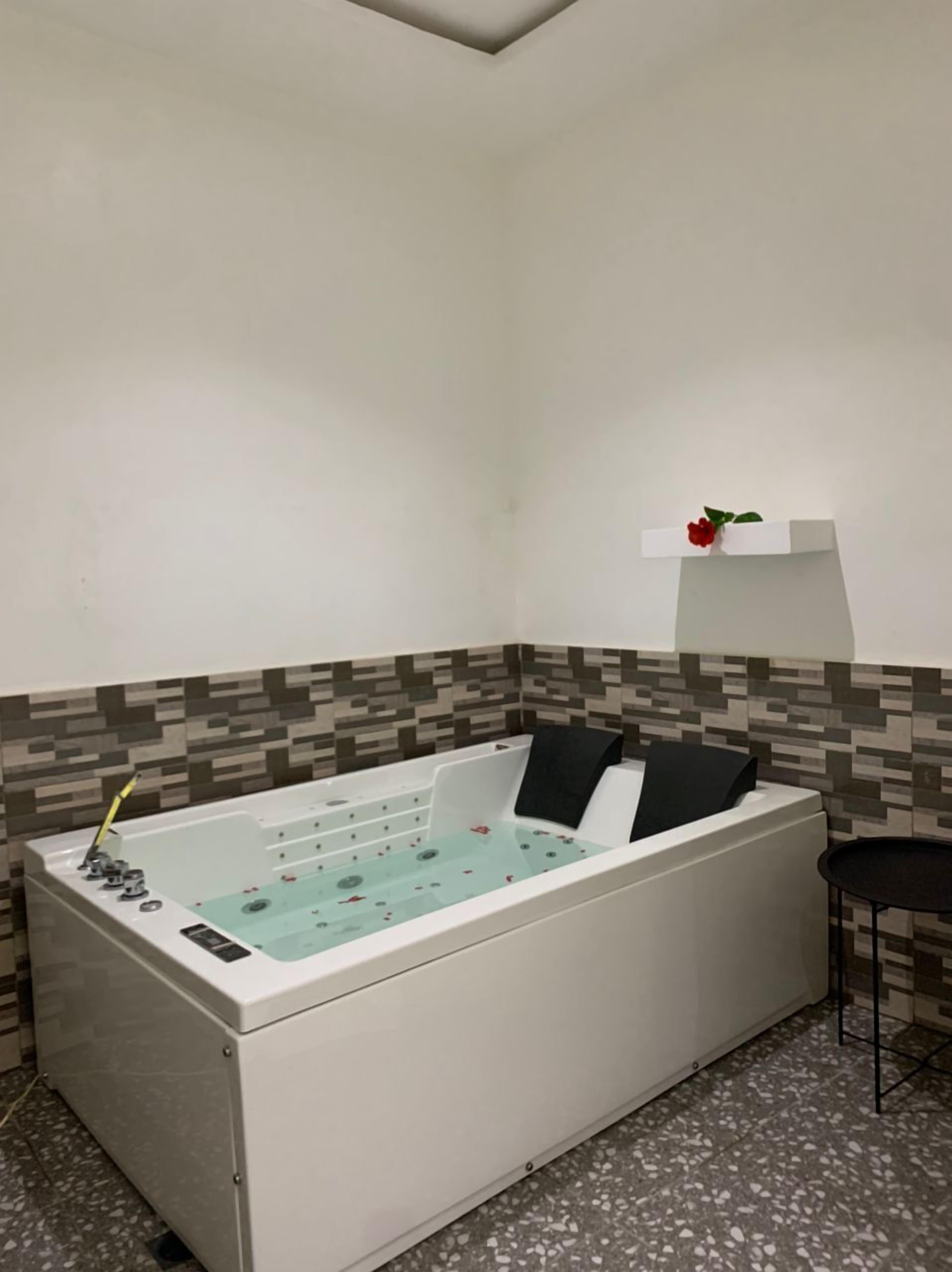 Un baño moderno con una bañera independiente, una mesita pequeña y una repisa decorativa con una flor.