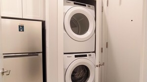 Une petite buanderie équipée d’un lave-linge et d’un sèche-linge à chargement frontal, d’un réfrigérateur et d’une porte dotée d’un porte-serviettes.