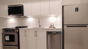 Une cuisine moderne avec des meubles blancs et des appareils en acier inoxydable, notamment un réfrigérateur, un lave-vaisselle, un four et un four à micro-ondes.