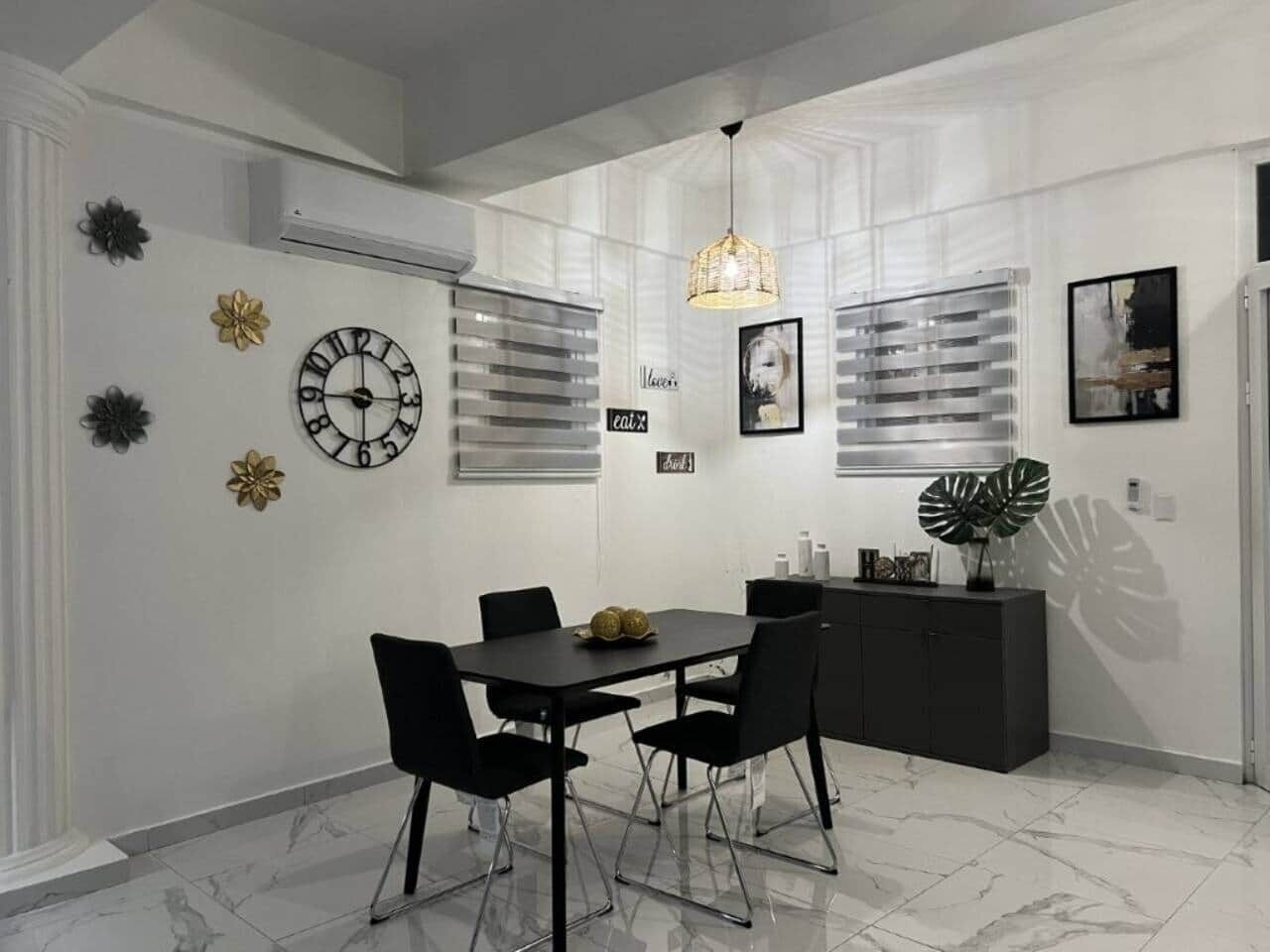 A modern dining area with a black table and chairs, a decorative clock, and a black cabinet with a plant.