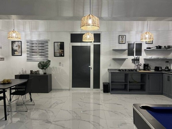 A modern kitchen with a dining area, featuring a marble floor, pendant lights, and a pool table.