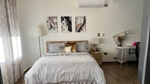 Une chambre à coucher comprenant un lit, des tables de chevet, un bureau et une chaise. Trois œuvres d’art sont accrochées au mur au-dessus du lit.