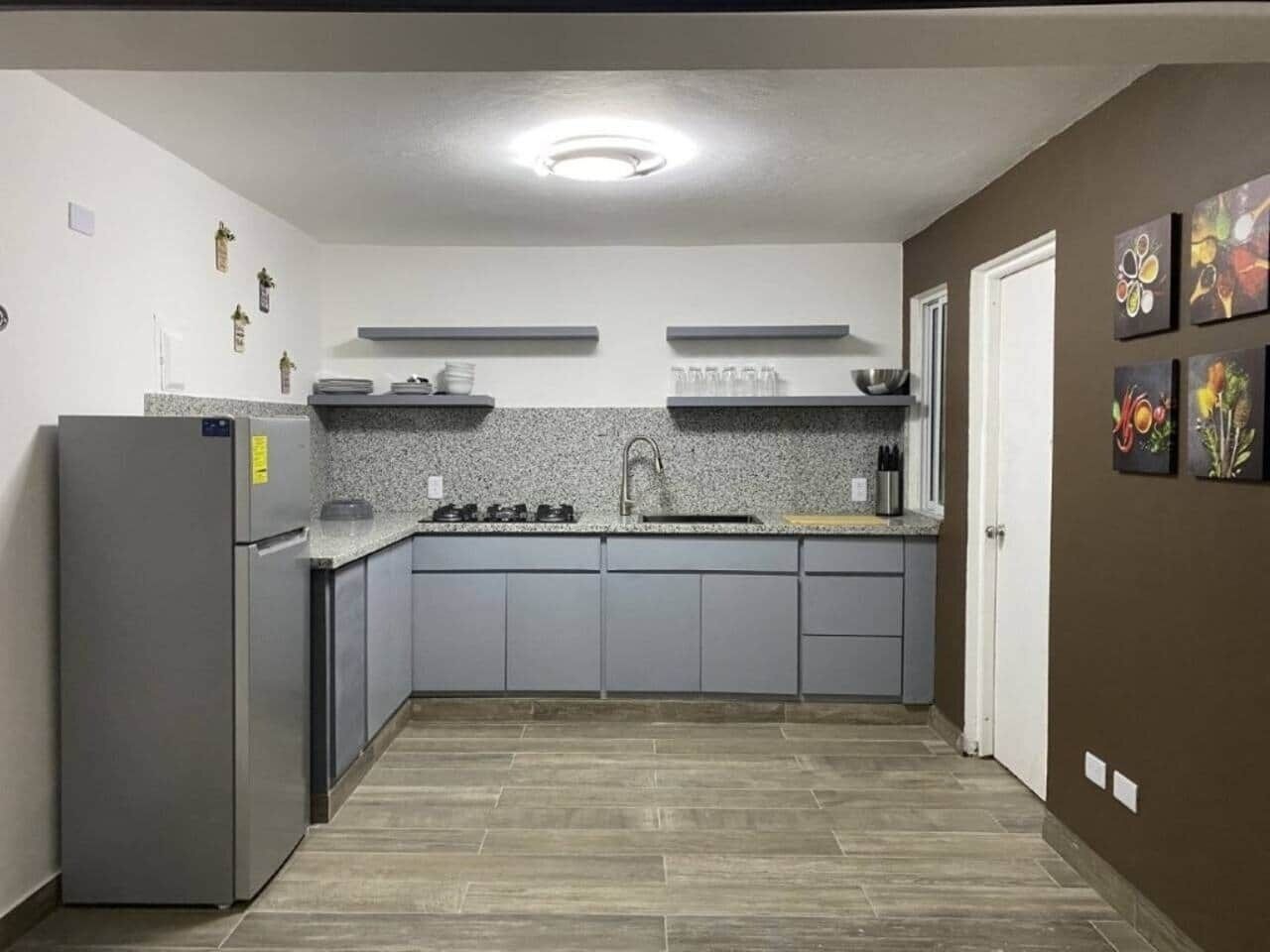 A compact kitchen with grey cabinets, a stainless steel refrigerator, a granite countertop, and a backsplash.