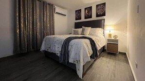 A modern bedroom with a large bed, a bedside table with a lamp, and a wall-mounted air conditioner. - The Driftwood Hideaway (Sosúa)