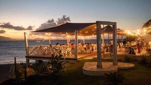 An outdoor restaurant with tables and chairs, a covered seating area, and a view of the sea. - The Driftwood Hideaway (Sosúa)