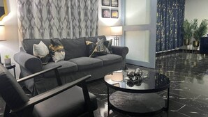 Un salon moderne avec un canapé gris, des fauteuils noirs, une table basse ronde noire et un rideau à motifs.