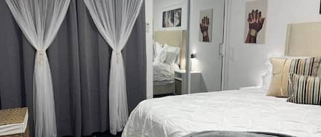 A bedroom with a bed, curtains, a bedside table, and a mirror.
