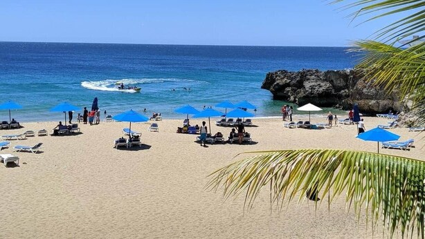 Une plage avec des chaises longues et des parasols, un promontoire rocheux et une eau d’un bleu limpide.