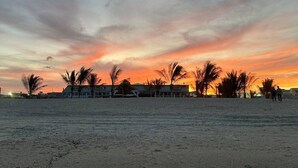 A beach with palm trees and a building in the background during sunset.