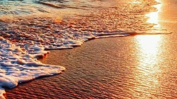 Escena de playa con olas y un atardecer.