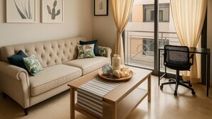 Un salón con un sofá color beige, una mesa de centro de madera, una silla de oficina negra y un balcón con barandilla.