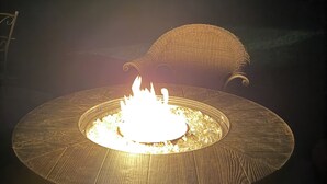 Una estructura redonda para fuego al aire libre, con llamas, rodeada por una silla de mimbre.
