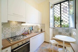 A compact kitchen with white cabinets, a gas stove, a sink, and a window with a metal grid.