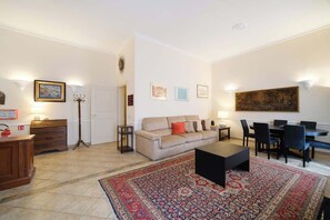 Ein Wohnzimmer mit Sofa, Couchtisch, Esstisch mit Stühlen, einem gemusterten Teppich und an der Wand befestigter Kunst.