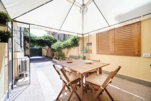 Un patio techado con una mesa y sillas de madera, un colgante de luz y vista a la calle.