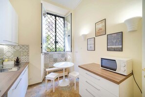 A compact kitchen with a window, a microwave, a sink, and a small dining area.