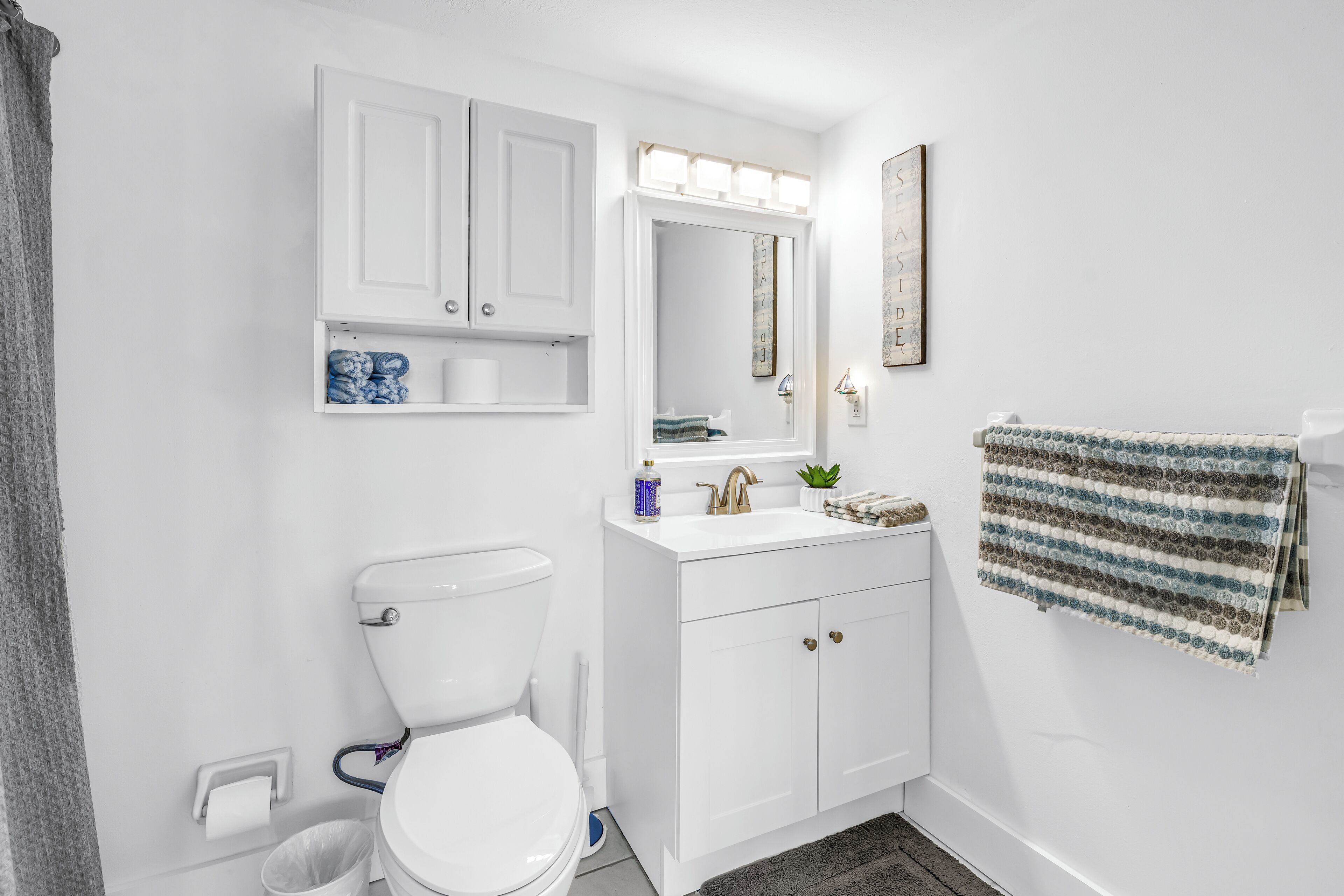 Une salle de bain avec des toilettes, des meubles blancs, un lavabo avec un miroir et une serviette accrochée au mur.