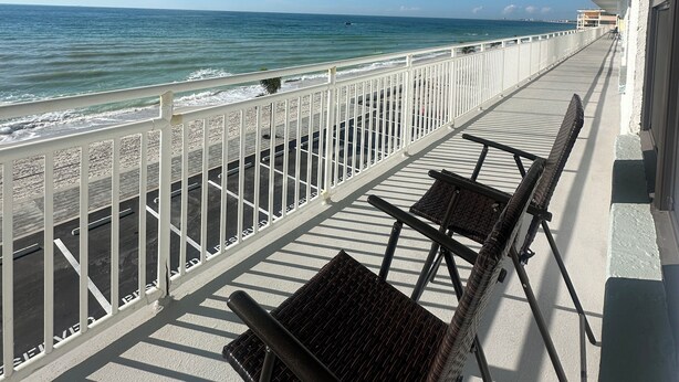A balcony with a view of the beach and ocean, featuring two wicker chairs and a white railing. - Sunset Beachfront Bliss
Wake Up to Waves & Gulf Views!
New heated Pool! (Treasure Island)