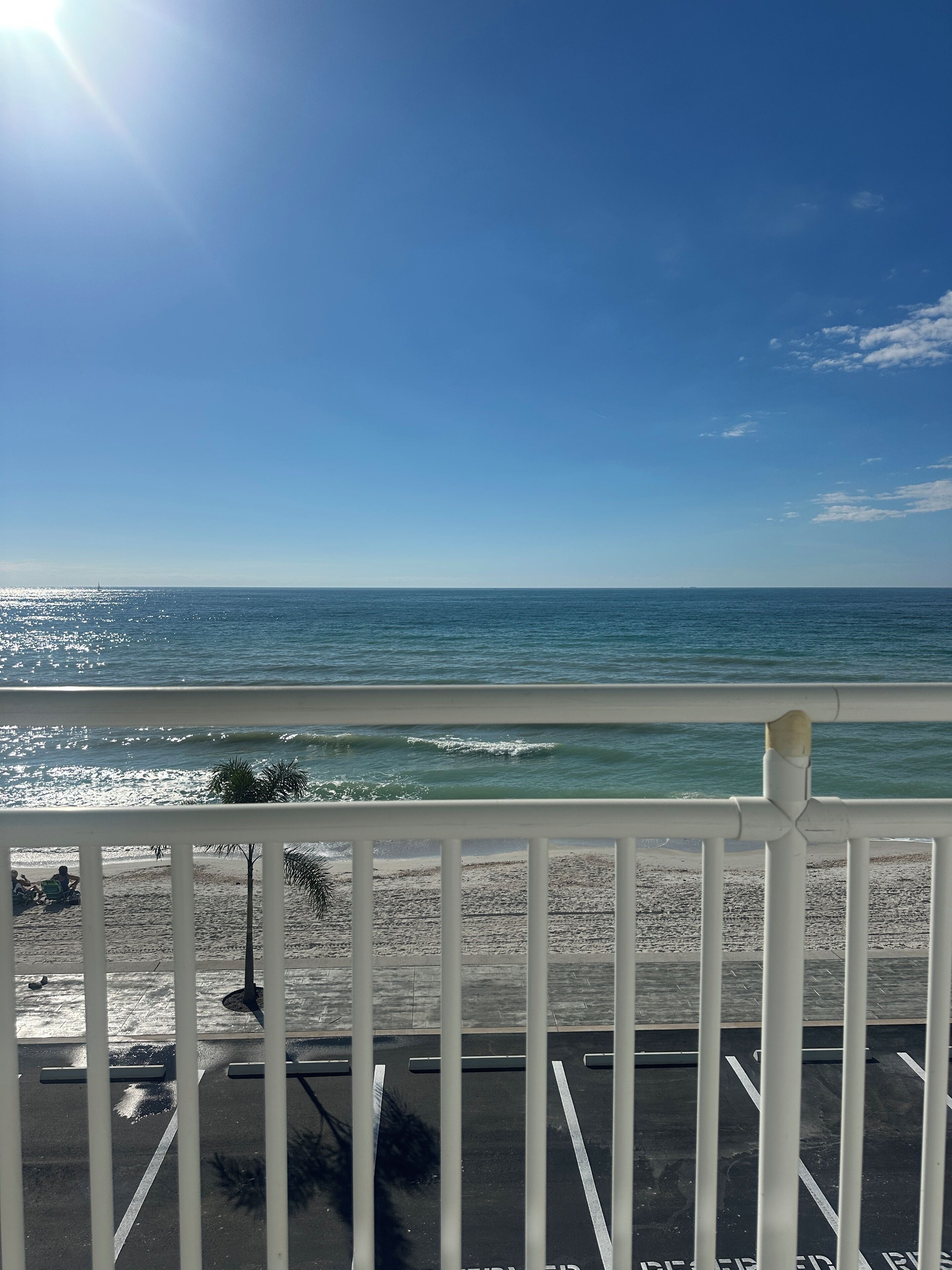 A view of the ocean from a balcony with a railing, a sandy beach, and a clear sky.
