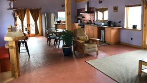 A spacious living area with a high ceiling, a dining table with chairs, a kitchen with wooden cabinets, and a large window providing natural light. - A Restful Retreat Just A Stones Throw Away From Downtown  (Quincy)