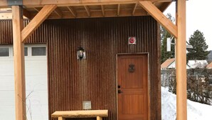 A wooden bench outside a building with a corrugated metal wall, a wooden door, and a small light fixture above the door. - A Restful Retreat Just A Stones Throw Away From Downtown  (Quincy)