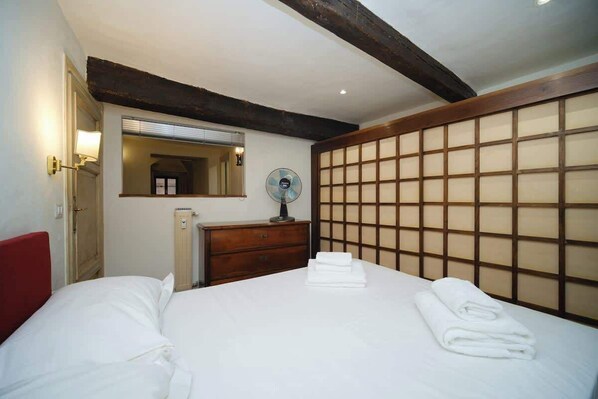 A hotel room with a bed, a dresser, a mirror, a fan, and a traditional Japanese-style partition.